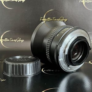 May include: A black camera lens with a silver ring and a black lens cap. The lens has a black rubber ring around the front.