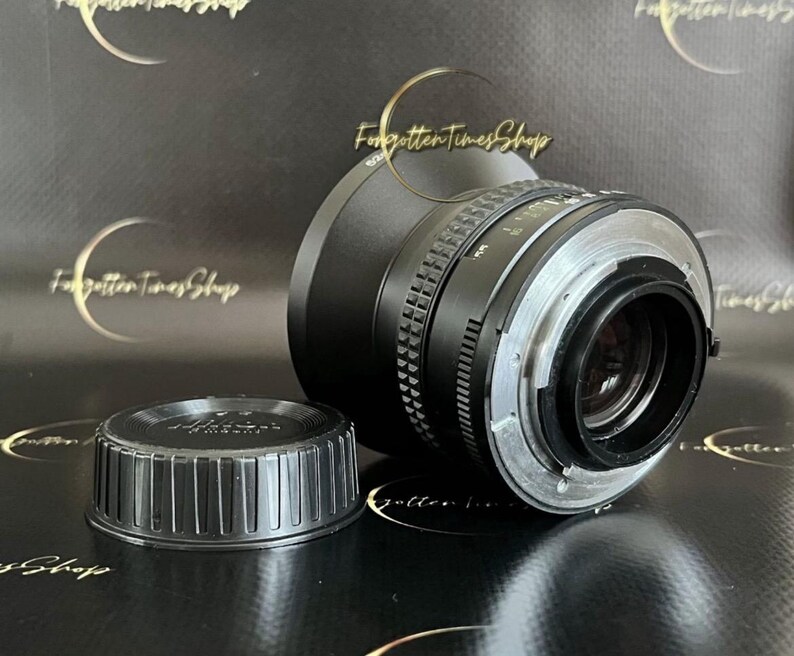 May include: A black camera lens with a silver ring and a black lens cap. The lens has a black rubber ring around the front.