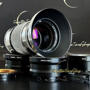 May include: A silver camera lens with a black lens cap. The lens has the text "ЮПИТЕР-37A" printed on it. The lens is surrounded by several black and silver camera adapters.