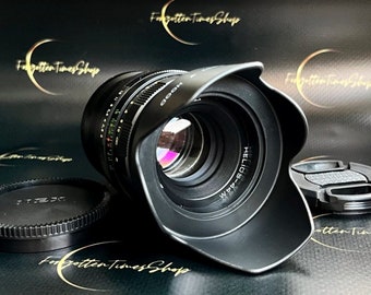 May include: A black camera lens with a lens hood attached. The lens has the text "HELIOS-44M" and "HOOD" printed on it.
