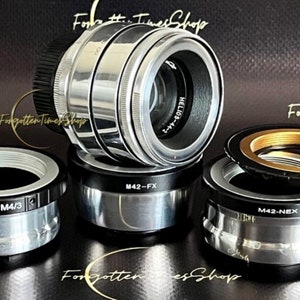 May include: Five silver and black camera lens adapters. The adapters are labeled "M42-FX", "M42-M4/3", "M42-NEX", and "HELIOS-44-2".