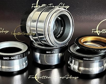 May include: Five silver and black camera lens adapters. The adapters are labeled "M42-FX", "M42-M4/3", "M42-NEX", and "HELIOS-44-2".