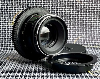 May include: A black camera lens with a silver ring around the front. The lens has a gear ring and the text "HELIOS-44-2" is printed on the front.