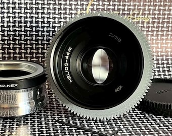 May include: A black and silver camera lens with a gear-like edge. The lens is labeled "HELIOS-44M" and "2/58".