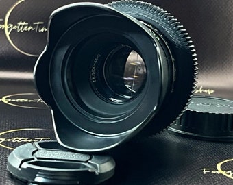 May include: A black camera lens with a lens hood attached. The lens has a gear ring and the text "Гелиос-44-2" printed on it.