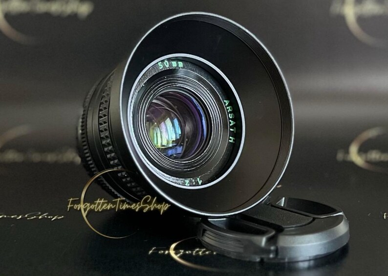 May include: A black camera lens with a silver ring around the edge. The lens has the text "ARSATH" and "50 mm 2.1" printed on it.