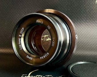 May include: A vintage camera lens with a metallic finish. The lens has markings including "F=300" and "1:10". The text "Made in USSR" is also visible. The lens is a classic piece of photography equipment.