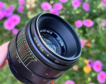 May include: A black camera lens with the text "HELIOS-44-2" and "2/58" printed on it. The lens has a silver ring around the edge and a series of numbers and markings on the side.