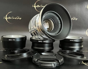 May include: A silver and black Helios-44M camera lens with a black lens hood, surrounded by black lens adapters and caps. The lens has the text "HELIOS-44M" and "M42-M4/3" printed on it. The background has the text "Forgotten Times Shop".
