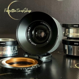 May include: A set of five camera lens adapters, including M42-NEX, M42-M4/3, M42-FX, and two additional adapters. The adapters are made of metal and have a silver finish. The lens adapters are used to connect different camera lenses to different camera bodies.