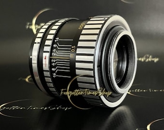 May include: A black and silver camera lens with a depth of field scale and a silver ring around the front. The lens has a black and silver M05 label.
