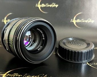 May include: A vintage Helios-44-2 camera lens with a black and silver body, and a Nikon lens cap. The lens has a series of colored markings and the text "HELIOS-44-2 2/58". The lens cap is black with the text "Nikon" on it.
