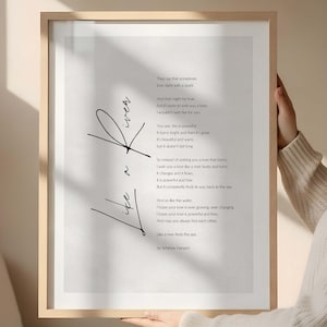May include: A framed art print with a light wood frame. The print displays a poem with the words "Like a River" in a stylized script. The poem is in black text on a white background.