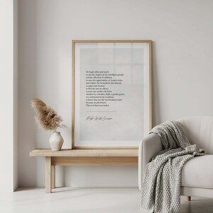 May include: A framed print with a light wood frame displays a poem in black text. The print rests on a light wood bench with a white vase and dried flowers. A white sofa with a gray blanket is to the right.