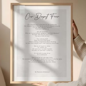 May include: A framed print with the title "Our Deepest Fear" in elegant script. The print features a poem by Marianne Williamson in a minimalist design, with a light-colored background and a wooden frame.