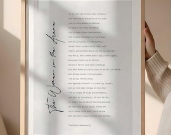 Op de afbeelding: Ingelijste print met de tekst "The Woman in the Arena" van Theodore Roosevelt. Het citaat staat in een handschrift op een witte achtergrond, in een licht houten frame. Een motiverend stuk.