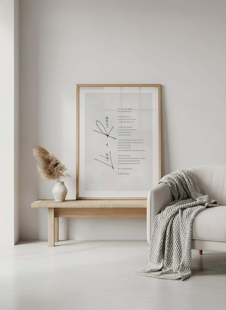 May include: A framed print with a poem in black script, titled "Life is". The artwork is displayed above a wooden bench with a vase of dried flowers. A white sofa with a gray knitted throw is to the right.