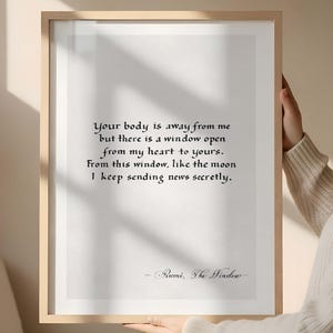 May include: A framed print with a light wood frame. The print features a poem by Rumi in elegant black script on a white background. The poem's title is "The Window". The frame is held by a person.