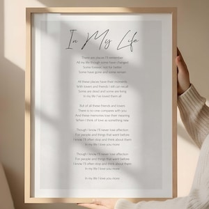May include: A framed print featuring the poem "In My Life". The text is in black script on a white background, with a light wooden frame. The poem speaks of memories and affection.