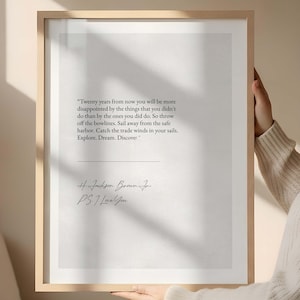May include: A framed print with a light wood frame. The print features a quote in black text: "Twenty years from now you will be more disappointed...Explore. Dream. Discover." The author's name and a closing are below the quote.