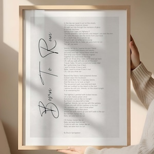 May include: A framed print featuring the lyrics to Bruce Springsteen's "Born to Run" in a handwritten style. The text is in black on a white background, with the title in a cursive font. The frame is a light wood color.