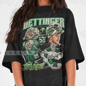 May include: Black oversized t-shirt with a vintage-style graphic of a hockey player wearing a green and white jersey with the name "DETTINGER" and the number "30" on the back. The graphic also includes the player's name "JAKE" in a stylized font.