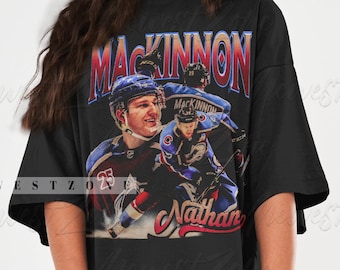 May include: Black oversized t-shirt featuring a graphic print of a hockey player wearing a blue and white jersey. The text "MACKINNON" is printed in red and yellow above the player and the text "Nathan" is printed in white below the player.