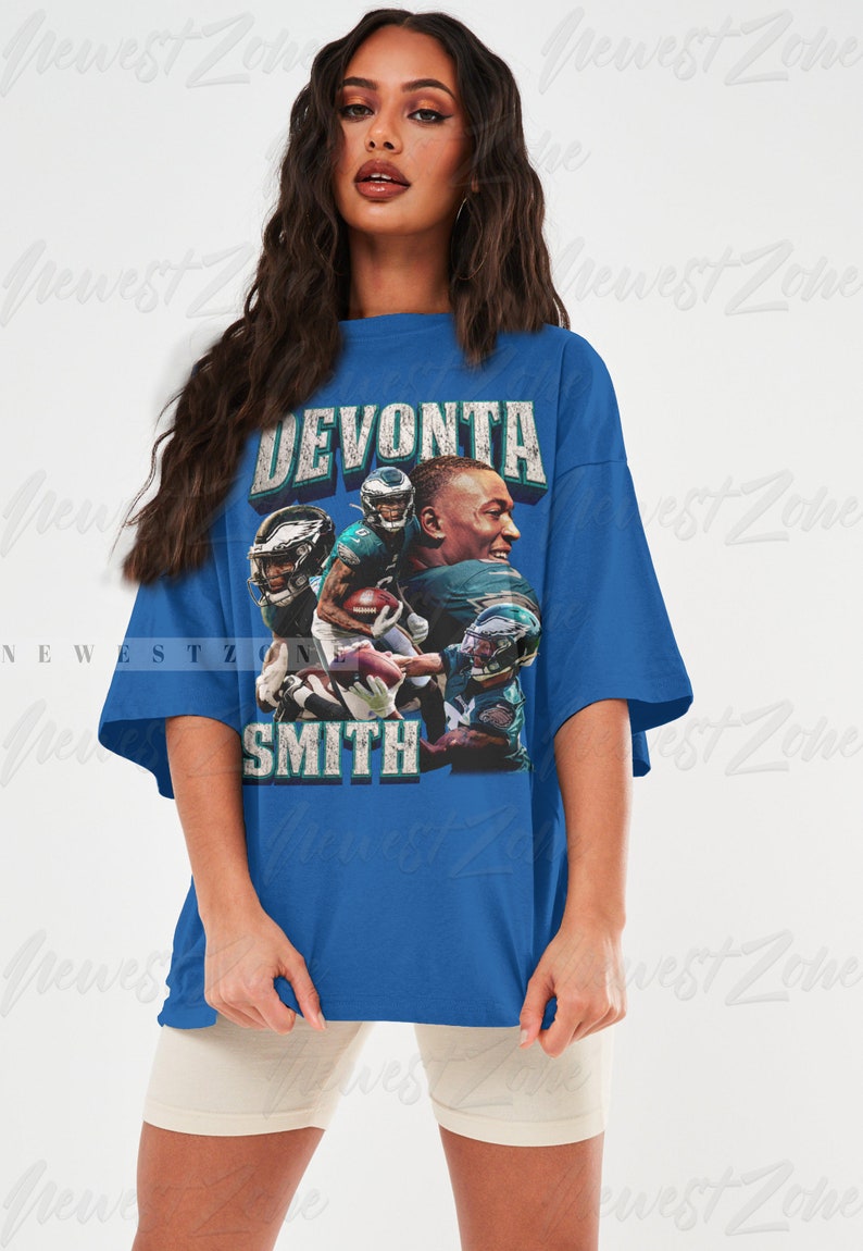 May include: A blue t-shirt featuring a graphic of football player DeVonta Smith. The design includes the player's name in distressed text and multiple images of him in action. The shirt is worn by a person.