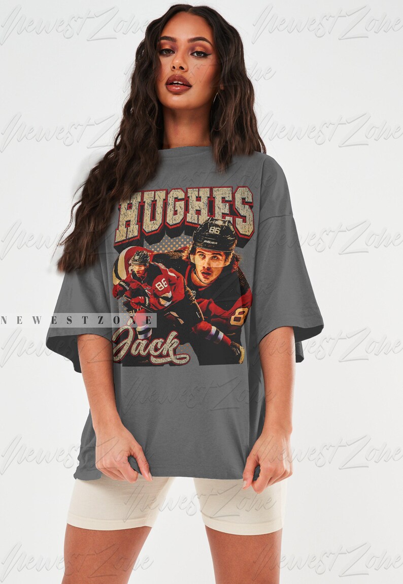 May include: A gray oversized t-shirt with a vintage-style graphic of a hockey player wearing a red and white jersey with the name "Hughes" and the number "86" on the back. The text "Jack" is printed below the graphic.
