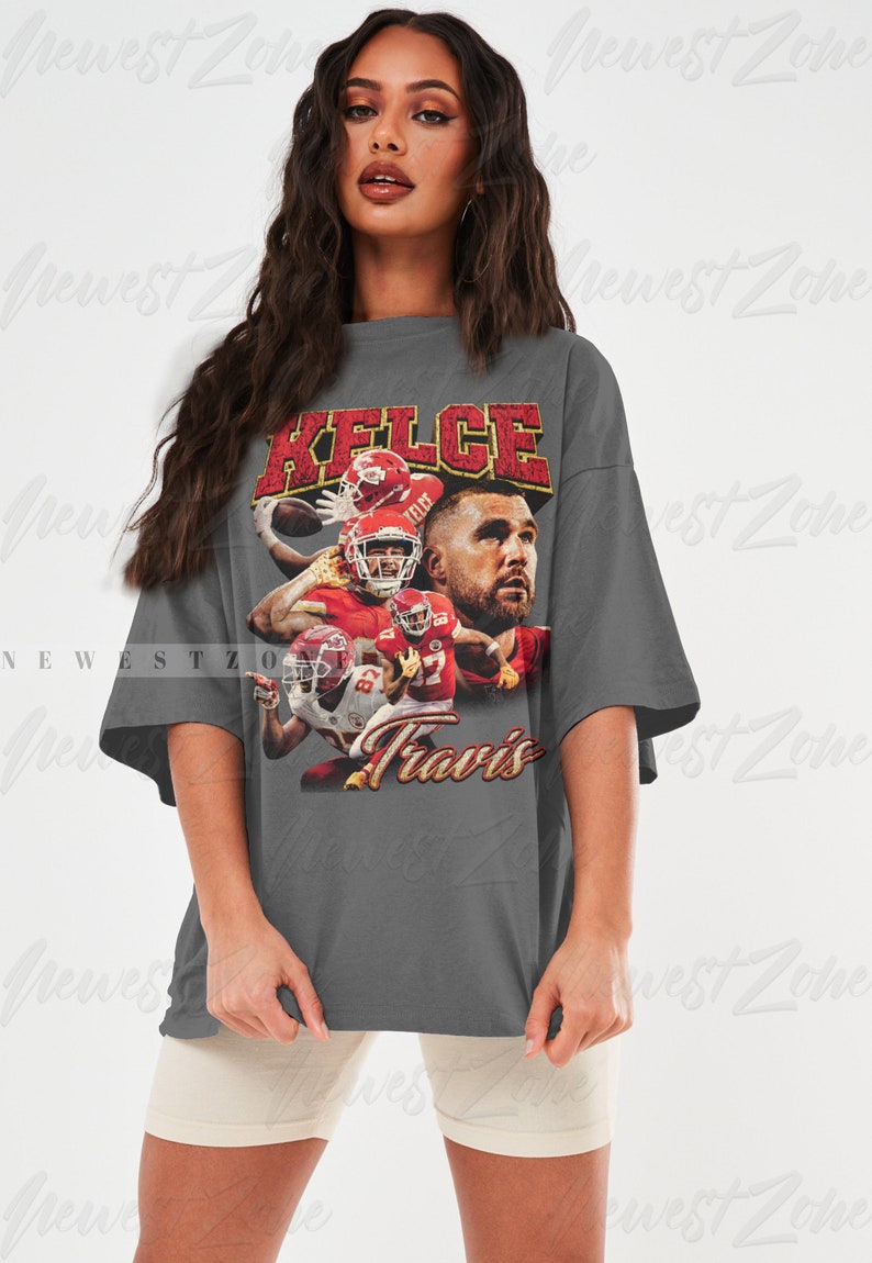 May include: Gray oversized t-shirt with a vintage-style graphic of a football player wearing a red jersey with the name "Kelce" and the number "87" printed on it. The text "Travis" is printed below the graphic.