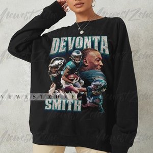 May include: Black sweatshirt featuring a graphic of Devonta Smith, with his name in a distressed font. The design includes images of Smith in his football uniform. The sweatshirt is a crew neck style.