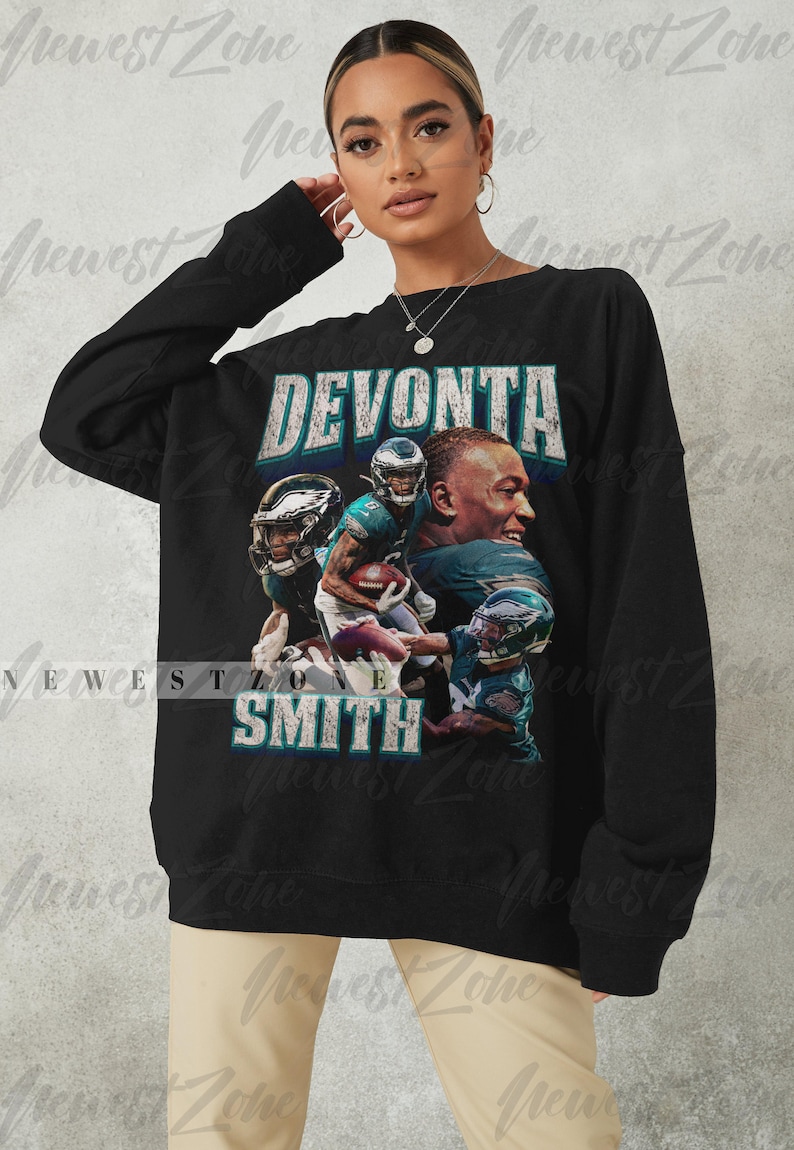 May include: Black sweatshirt featuring a graphic of Devonta Smith, with his name in a distressed font. The design includes images of Smith in his football uniform. The sweatshirt is a crew neck style.