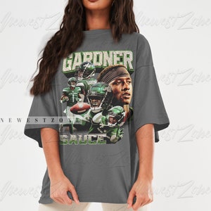 May include: An oversized grey t-shirt featuring a vintage-style graphic of a football player wearing a green and white jersey. The text "GARDNER" and "SAUCE" is printed on the shirt.