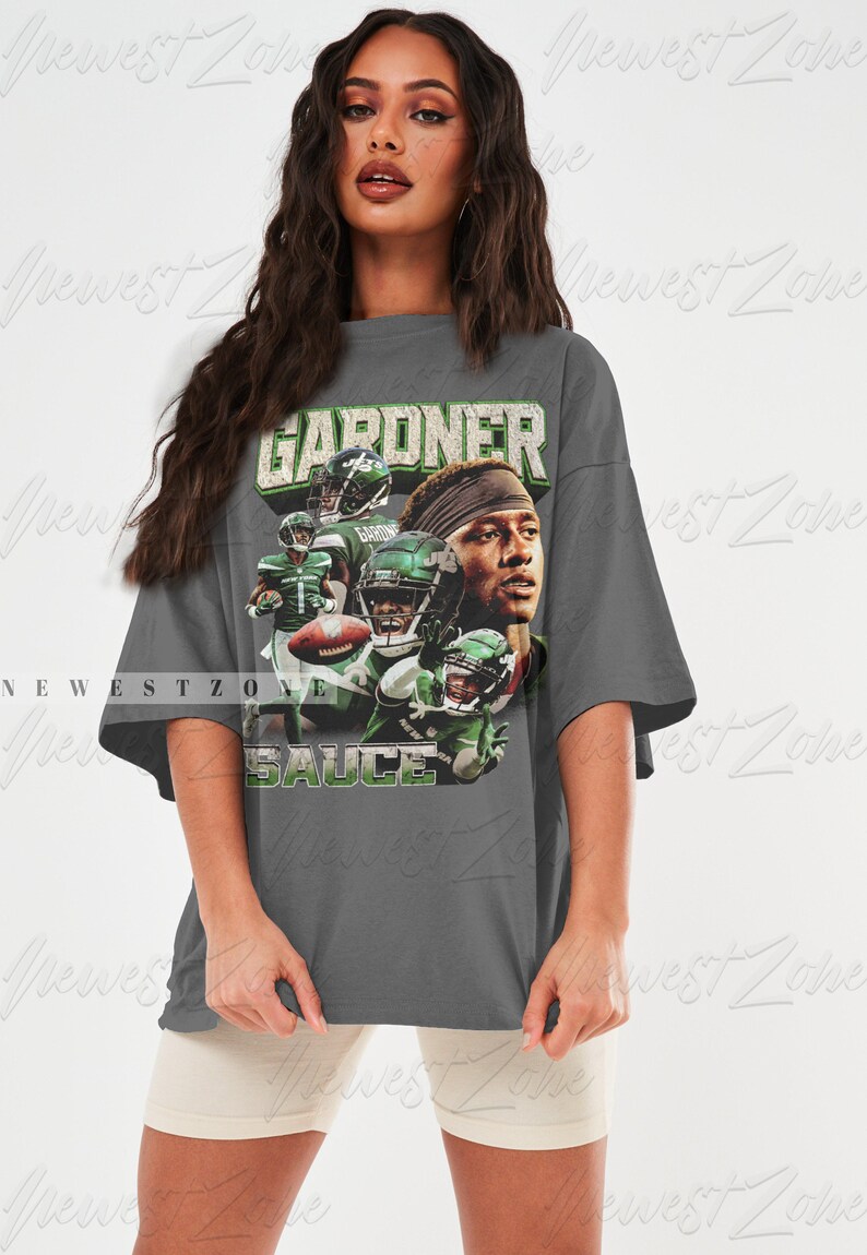 May include: An oversized grey t-shirt featuring a vintage-style graphic of a football player wearing a green and white jersey. The text "GARDNER" and "SAUCE" is printed on the shirt.