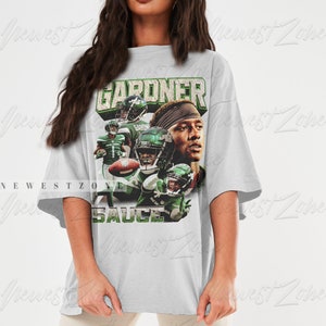 May include: An oversized grey t-shirt featuring a graphic print of a football player wearing a green and white jersey with the text "GARDNER" and "SAUCE".
