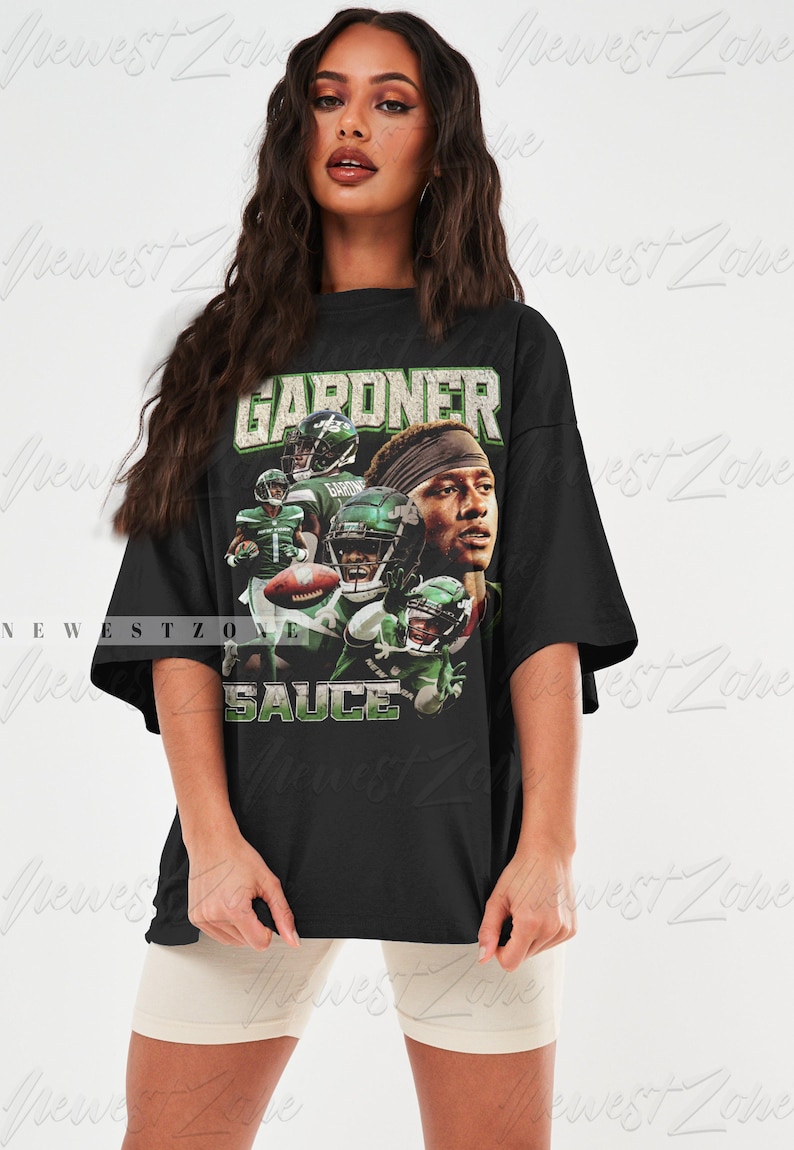 May include: Black t-shirt featuring a graphic print of a football player wearing a green and white jersey. The text "GARDNER" and "SAUCE" is printed on the shirt.