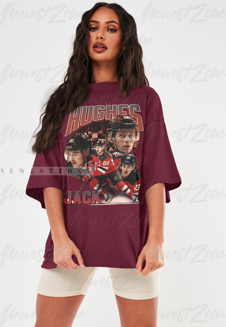 Puede incluir: Una camiseta de gran tama&ntilde;o de color granate con un gr&aacute;fico de estilo vintage de jugadores de hockey. El gr&aacute;fico incluye el texto "HUGHES" y "JACK" y el n&uacute;mero "86".