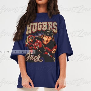 May include: A navy blue oversized t-shirt with a vintage-style graphic of a hockey player wearing a red and white jersey with the number 86. The text "HUGHES" and "Jack" are printed on the shirt.