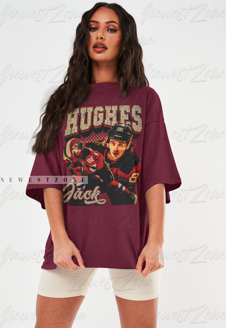 May include: A maroon t-shirt with a vintage-style graphic of a hockey player wearing a red and white jersey with the number 86 on it. The text "HUGHES" and "Jack" are printed on the shirt.