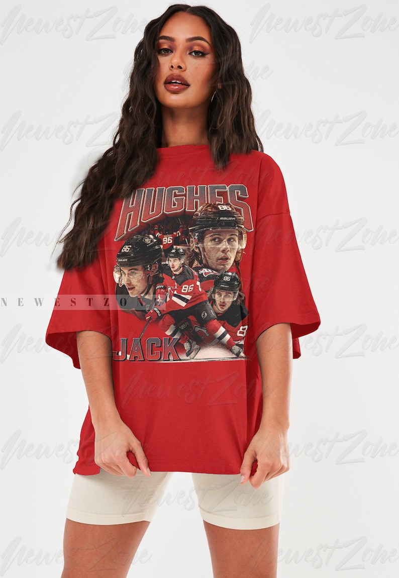 Puede incluir: Camiseta roja de gran tama&ntilde;o con un gr&aacute;fico de estilo vintage de jugadores de hockey que llevan camisetas rojas y blancas. El gr&aacute;fico incluye el texto "HUGHES" y "JACK".