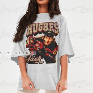 May include: A gray oversized t-shirt with a vintage-style graphic of a hockey player wearing a red and white jersey with the text "HUGHES" and "Jack" on the shirt.