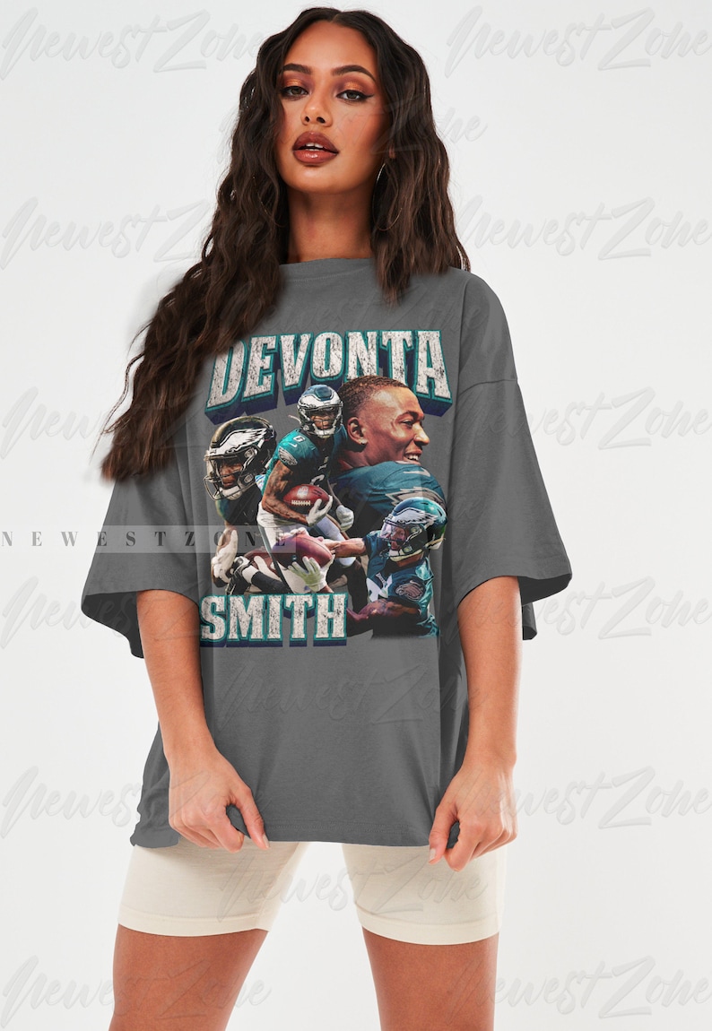 May include: A gray t-shirt featuring a graphic of football player DeVonta Smith. The design includes images of the player in action, with the name "DEVONTA SMITH" in a distressed font. The shirt is a casual, oversized style.