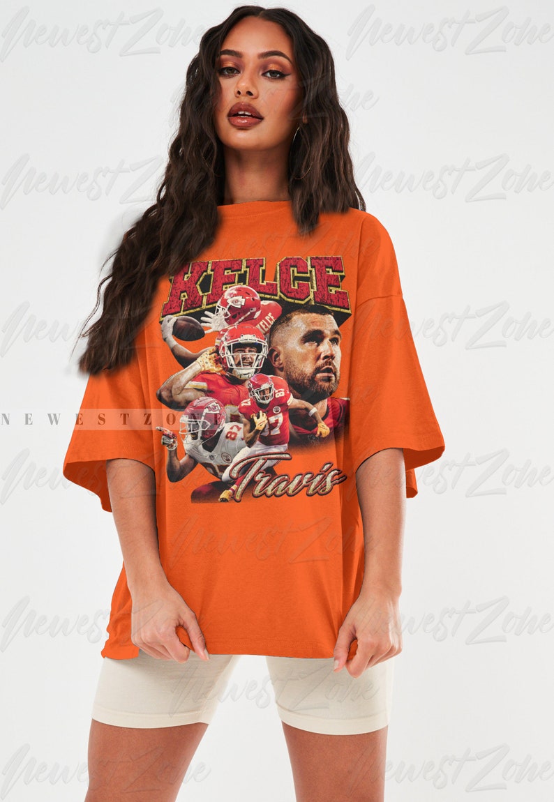 May include: Orange oversized t-shirt with a vintage-style graphic of Travis Kelce, a football player for the Kansas City Chiefs. The graphic features Kelce in action with the text "Kelce" and "Travis" printed on the shirt.