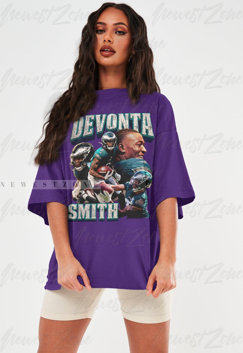 May include: A purple t-shirt featuring a graphic of Devonta Smith, with the text "DEVONTA SMITH" in a distressed font. The graphic includes images of Smith in an Eagles uniform. The shirt is oversized.