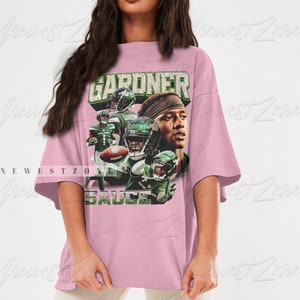 May include: An oversized pink t-shirt featuring a graphic print of a football player wearing a green and white jersey. The text "GARDNER" and "SAUCE" are printed on the shirt.