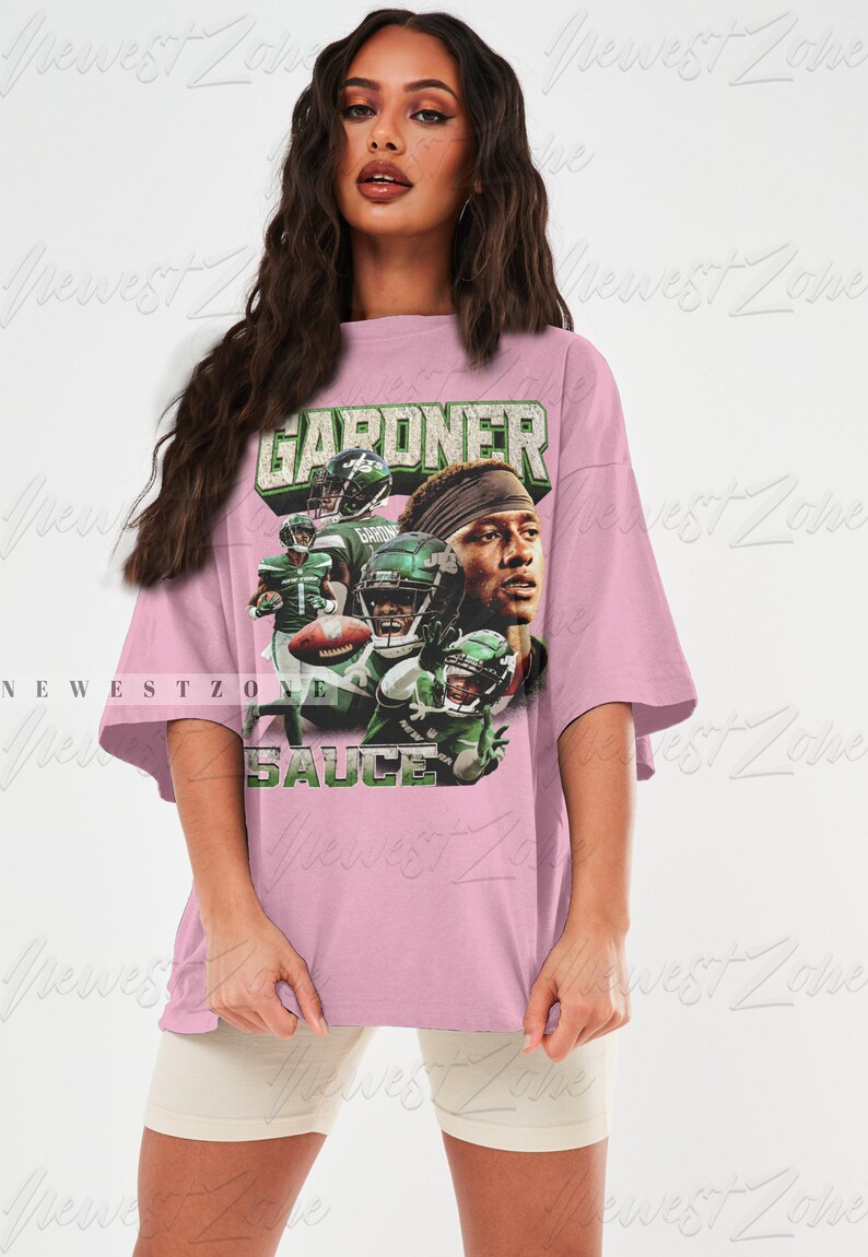 May include: An oversized pink t-shirt featuring a graphic print of a football player wearing a green and white jersey. The text "GARDNER" and "SAUCE" are printed on the shirt.