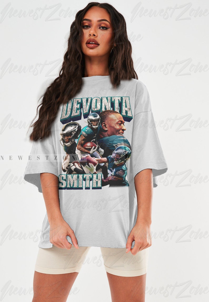 May include: White t-shirt featuring a graphic of football player DeVonta Smith. The design includes the player's name in a distressed font, along with images of him in action. The shirt has short sleeves and a relaxed fit, suitable for casual wear.