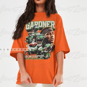 May include: Oversized orange t-shirt featuring a graphic print of a football player wearing a green and white jersey with the text "GARDNER" and "SAUCE" on the shirt.