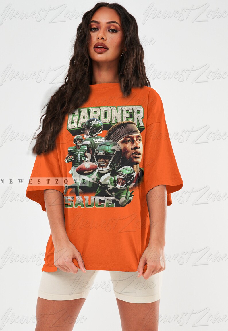May include: Oversized orange t-shirt featuring a graphic print of a football player wearing a green and white jersey with the text "GARDNER" and "SAUCE" on the shirt.