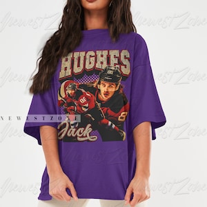 May include: Purple oversized t-shirt with a vintage graphic of a hockey player wearing a red and black jersey with the text "HUGHES 86" on the back of the jersey. The text "Jack" is printed below the graphic.
